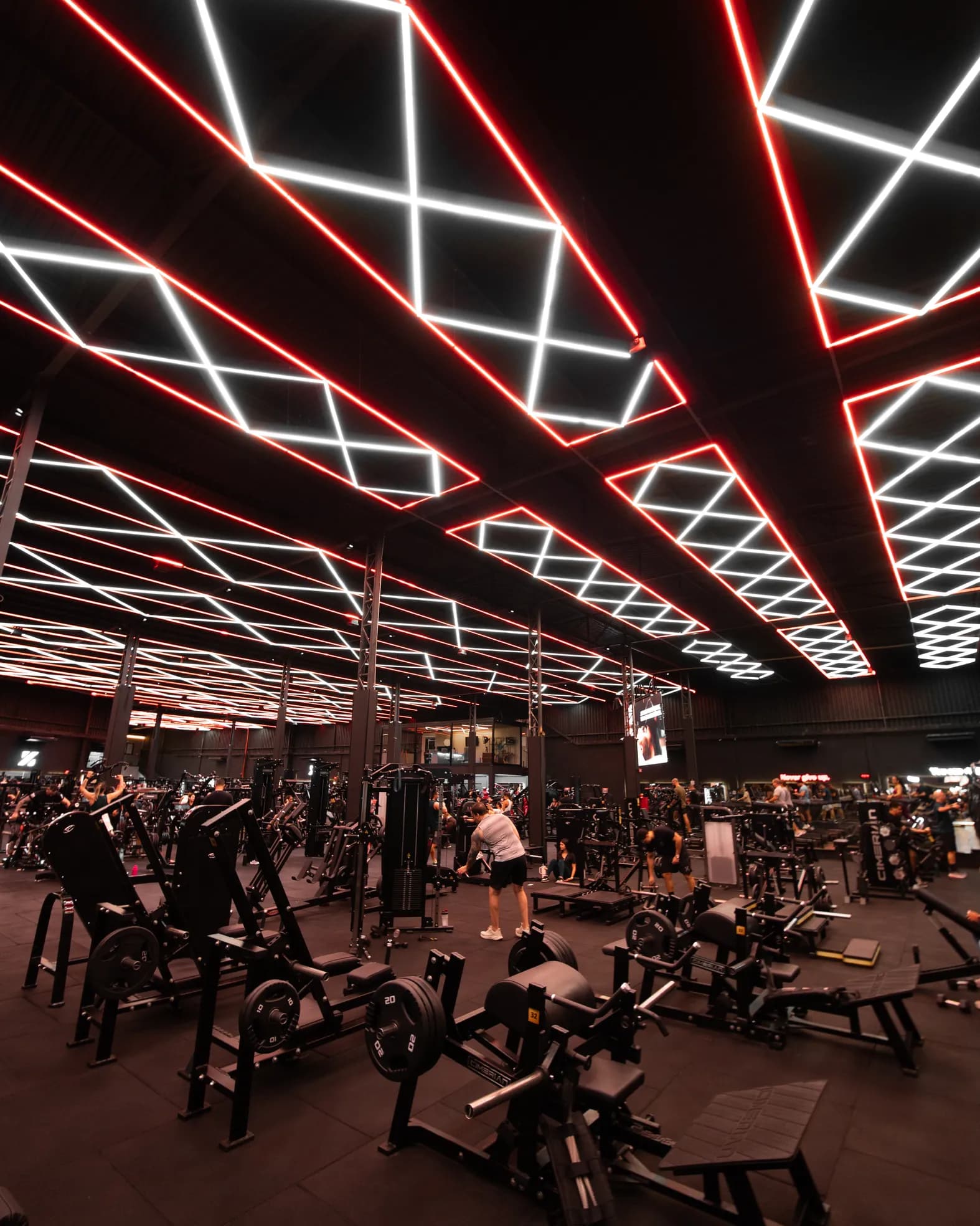 Salão da Iron Zone visto em perspectiva, com o teto de LED se estendendo sobre as estações e os sócios treinando