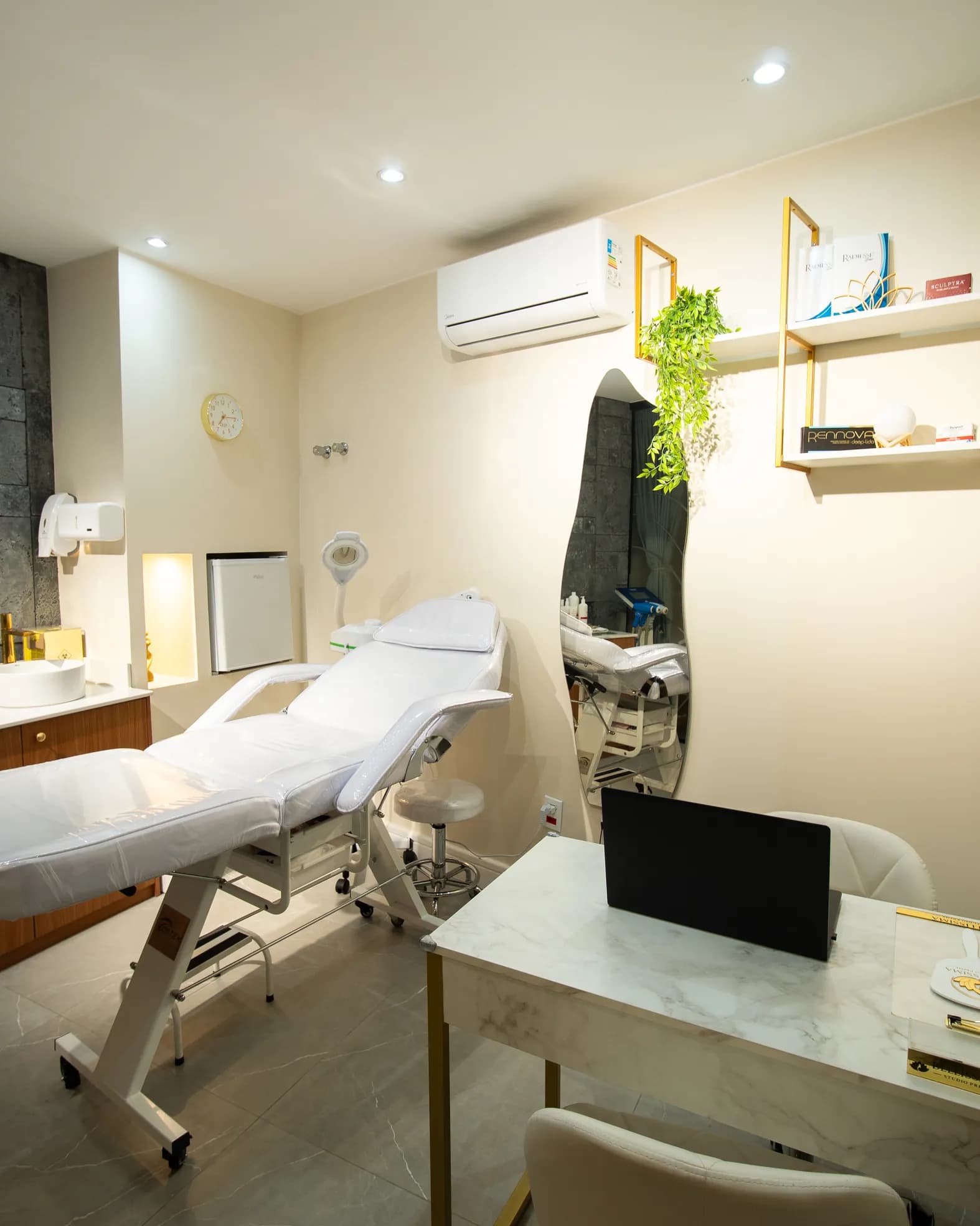 Sala de estética com maca branca, bancada e prateleiras douradas