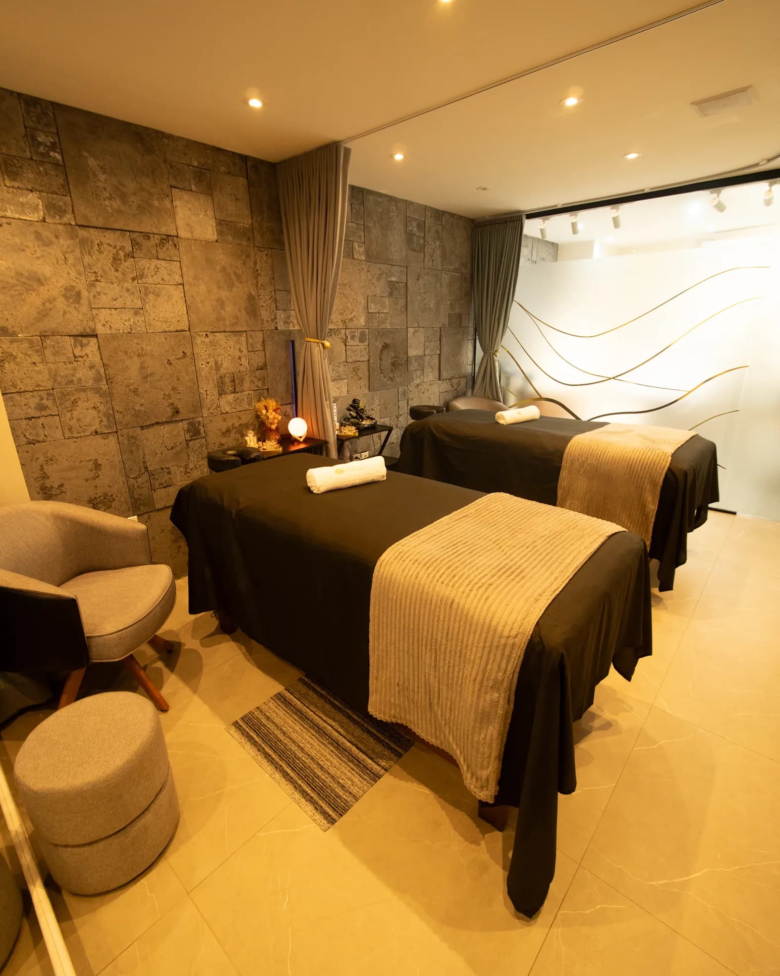 Sala de massagem do spa com duas macas e parede de pedra