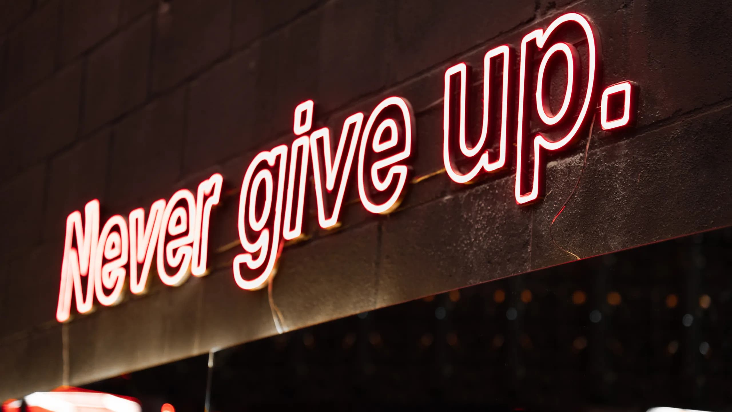Letreiro de neon na parede da Iron Zone com a frase "Never give up."